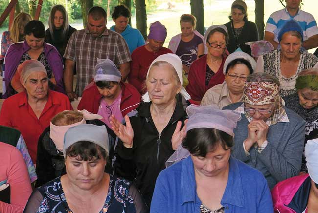 Moldovan women, with their hair tied in kerchiefs, gather under an outdoor portico for a prayer conference.