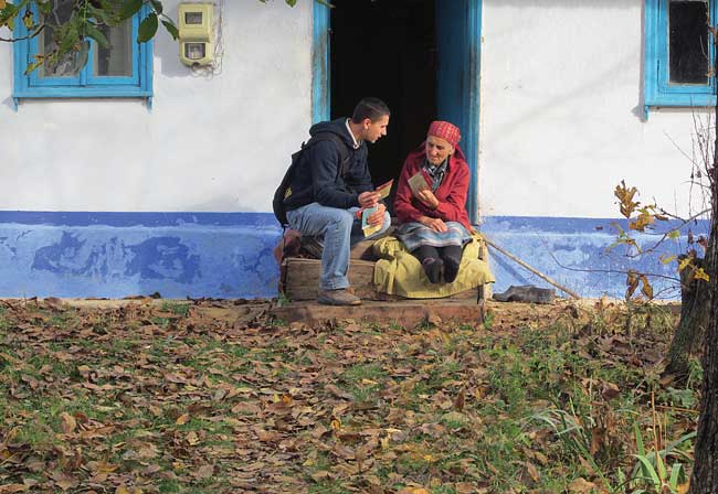 A pioneer missionary sits with an elderly woman on the steps of her rural home to share the Gospel.