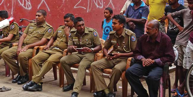 Uniformed Sri Lankan Policemen sit in a row of chairs to watch a presentation.