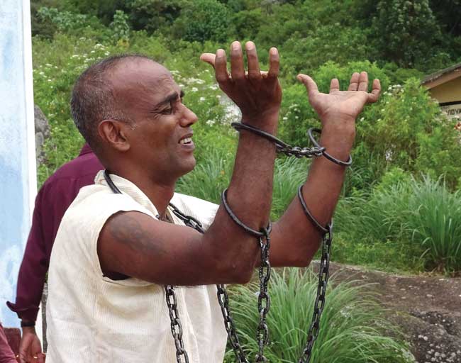 An actor dressed as a prisoner raises his hands in chains.
