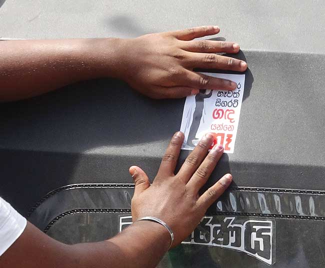 Hands post a sticker advertising the street drama team on a car.